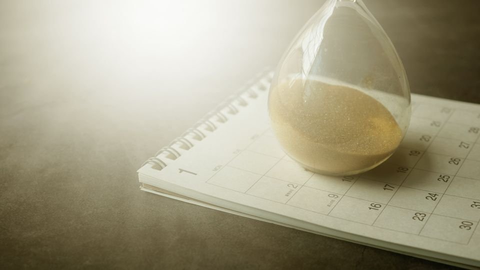 Ampulheta sobre calendário representando passagem do tempo e decisões adiadas.
