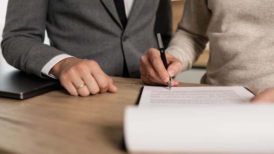 Pessoas assinando documentos em uma mesa de reunião.