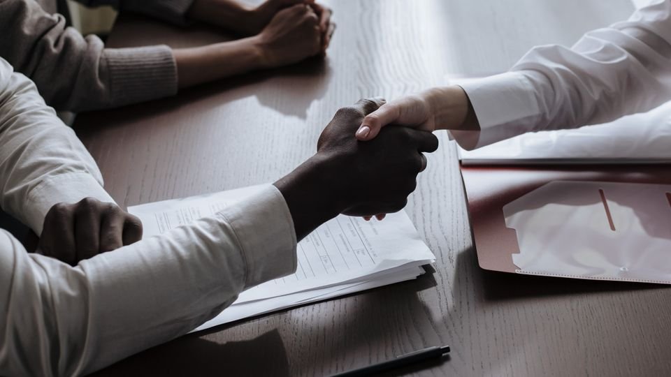 Aperto de mãos sobre documentos de contrato durante uma negociação.