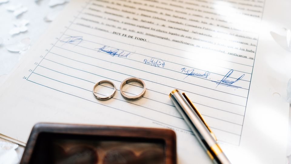 Alianças sobre uma certidão de casamento assinada.